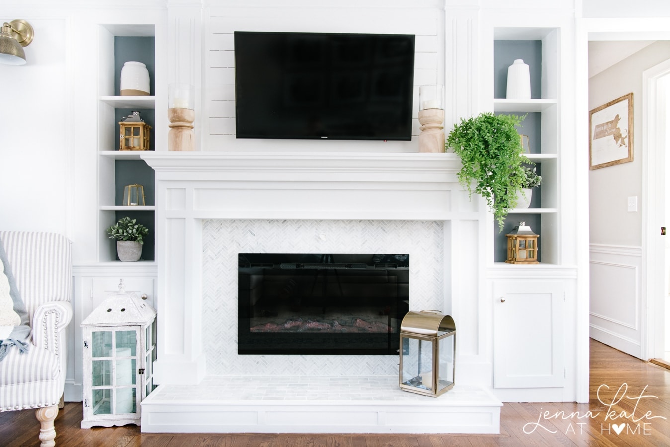 A fireplace with white mantle, wall-mounted television and built-in shelves on either side