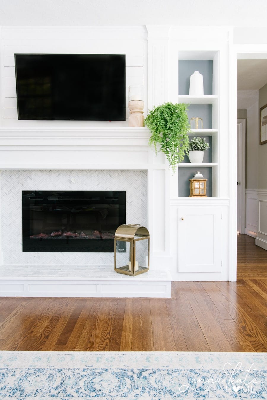 A fireplace in a living room with a wall-mounted television and miscellaneous decor items on the adjacent built-in shelf 