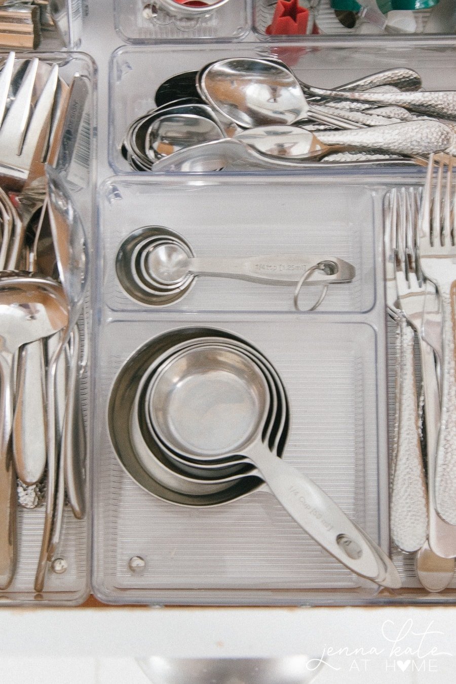 A kitchen cabinet with dividers storing silverware, measuring cups, measuring spoons, and more.