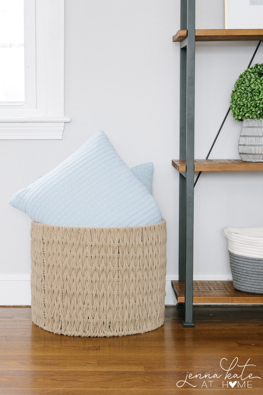 A large wicker basket holding light blue throw pillows