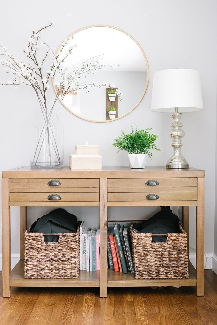 A wooden console table with four narrow drawers, and a shelf below holding 2 large wicker baskets