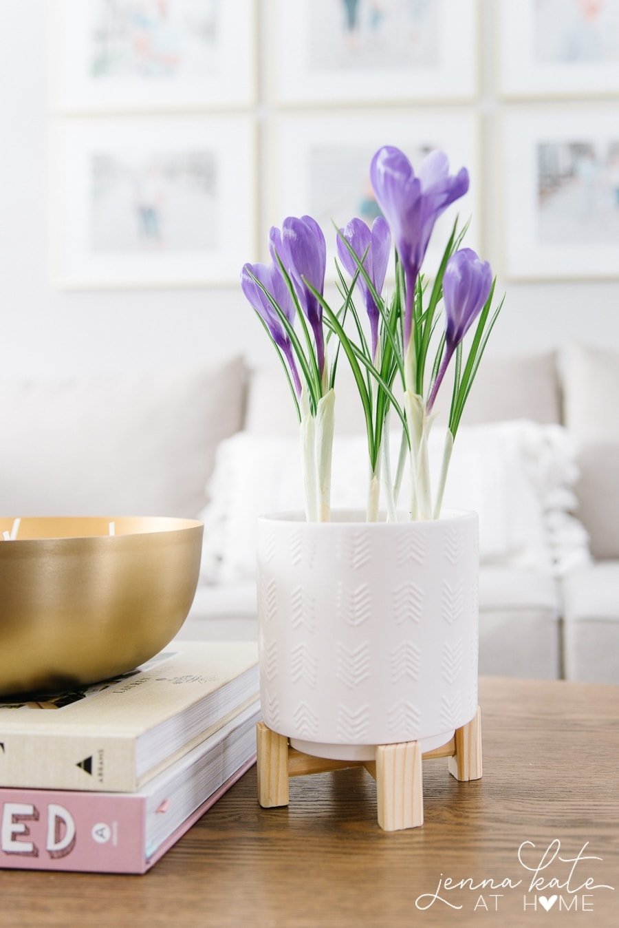 Purple flowers in a white ceramic pot with wooden pedestals near a stack of books