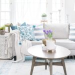 A living room containing a light grey sofa with various blue throw pillows, near a wooden coffee table