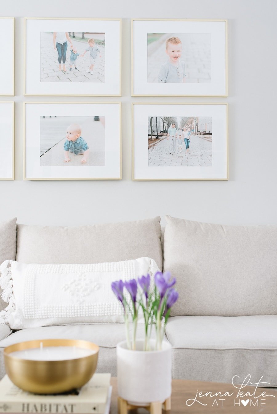 Purple flowers in a white pot, on a wooden coffee table in front of a light grey sofa