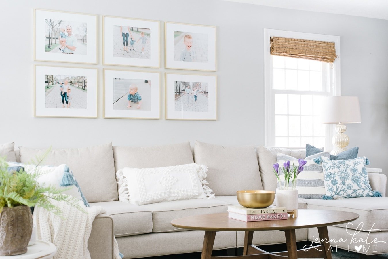 A light grey sofa and oval, wooden coffee table under a collection of family portraits