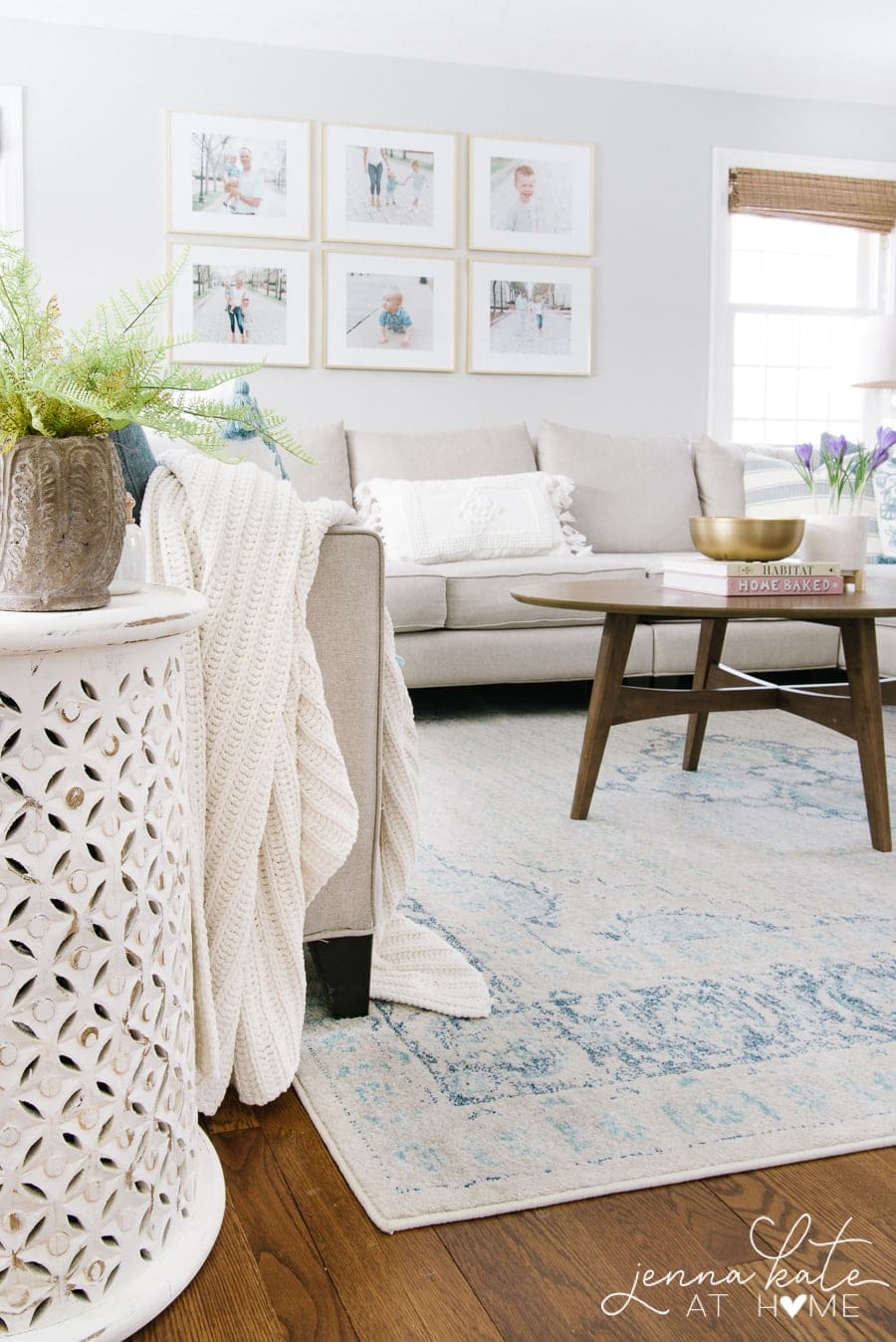 A side view of the living room, with a closer look at a side table with diagonal patterns on the side, holding a brown vase of greenery