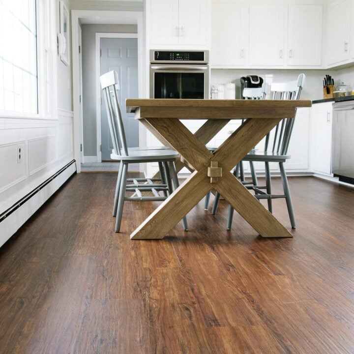 A wooden dining table and chairs resting on newly-installed wide, brown luxury vinyl planks