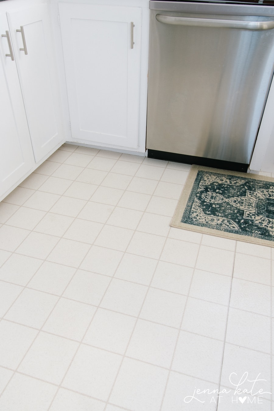 The white tile floor of a kitchen, with a blue and white rug near the dishwasher/sink area