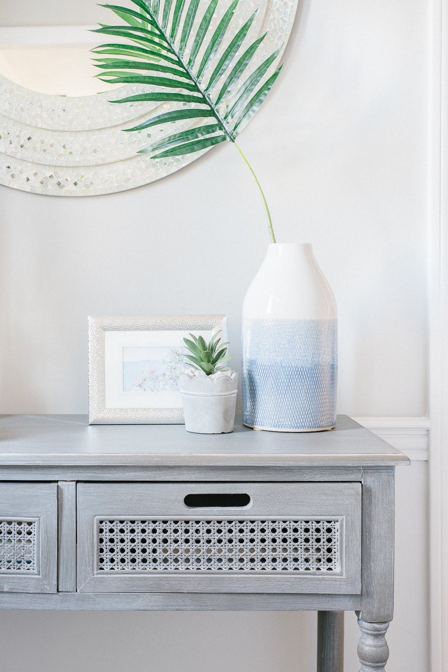 A wooden, grey console table with a gradient blue patterned jug, plant in a small white pot and a photo in a light grey frame