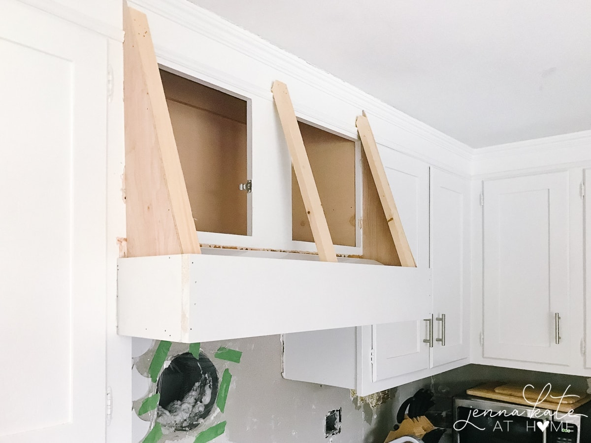 The wooden sides and sloping strips of wood attached to an upper cabinet as a framework for the hood cover