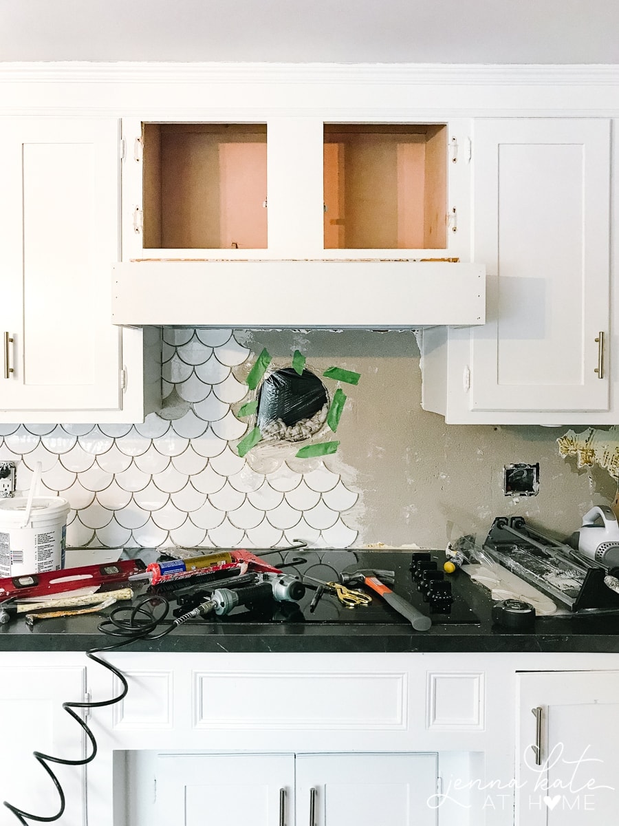 Work in progress: an upper cabinet with doors removed, awaiting a new hood cover, while tools rest on the stovetop below