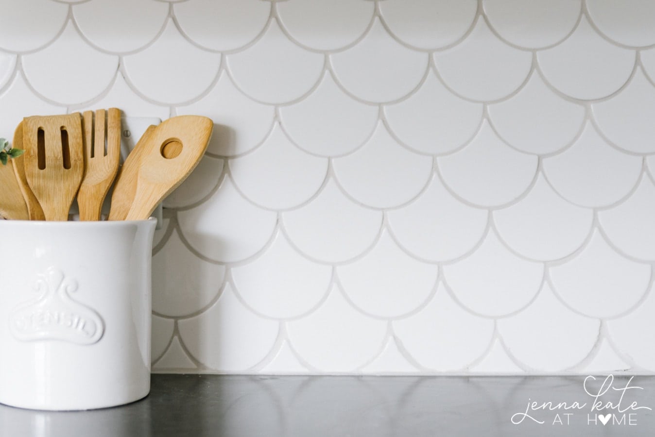 White shell-patterned tile backsplash with a pot of wooden utensils nearby