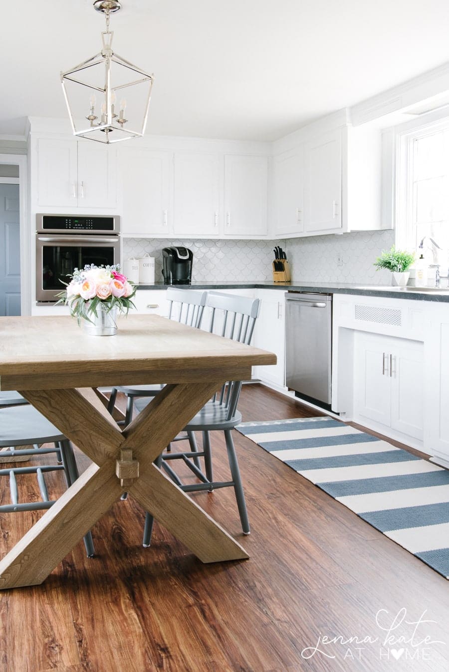 A wooden table and chairs in a kitchen with dark, wood floors and blue/white rug