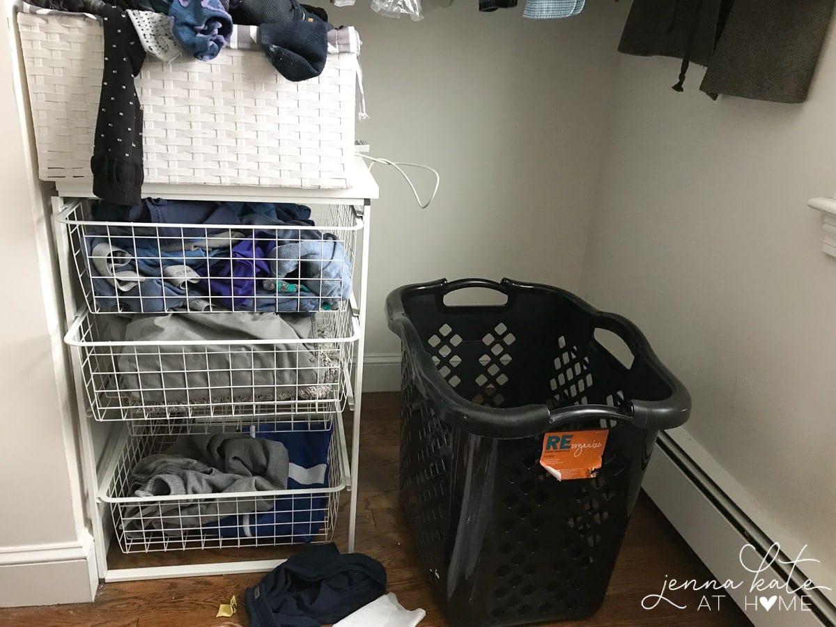 A 3-drawer wire rack, white basket and black laundry hamper resting in a room