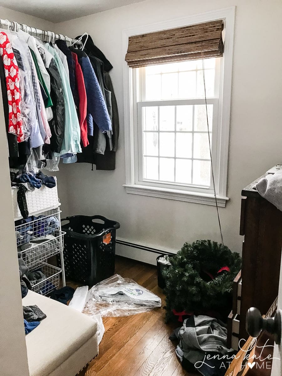 Clothes hanging on a rod near a window, above a wire rack of other clothing, with miscellaneous items resting nearby