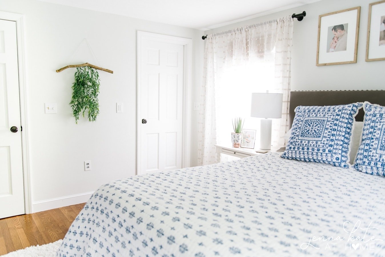 Photo of bedroom, with branch wall hanging near door, near bed with blue and white coverlet & pillows