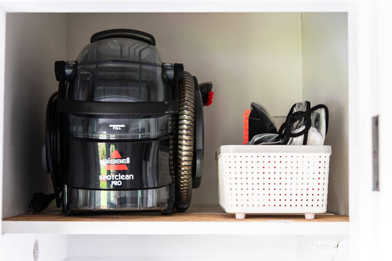 The new top shelf holding a vacuum canister and smaller parts of a vacuum in a white basket