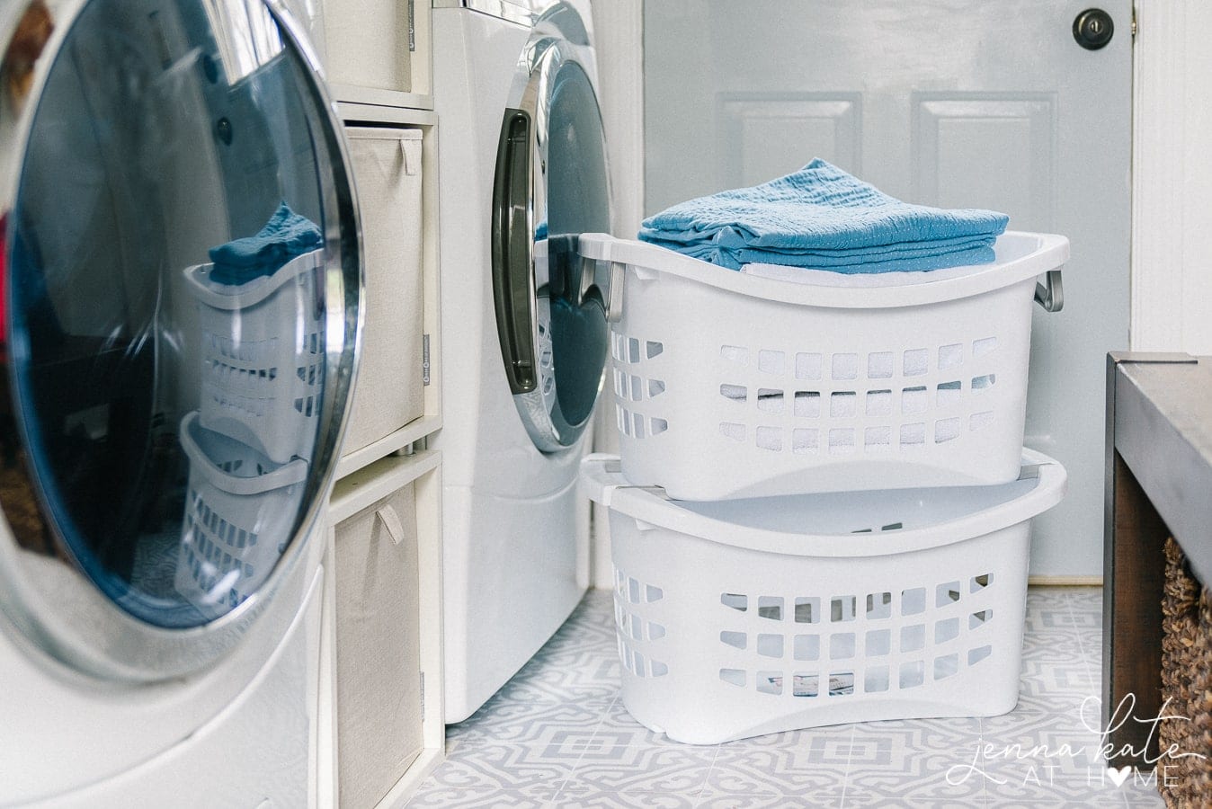 2 white laundry baskets stacked on top of each other in front of a washer and dryer in the mudroom