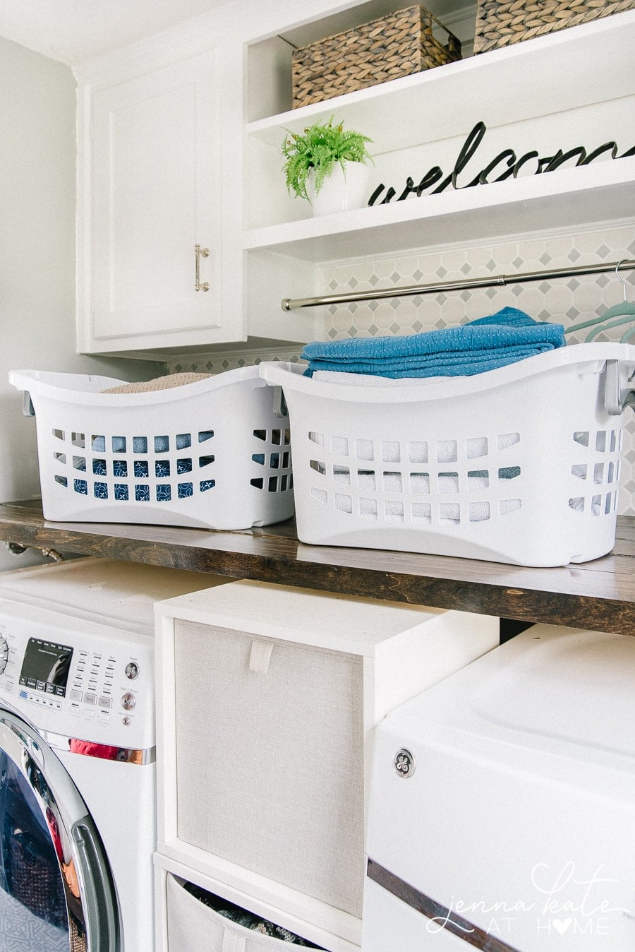 Two white laundry baskets sitting on a new shelf in the laundry room, above the washer and dryer.
