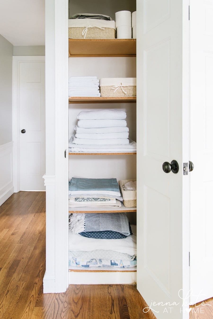 A linen closet with four shelves containing towels, sheets and assorted blankets/throws.