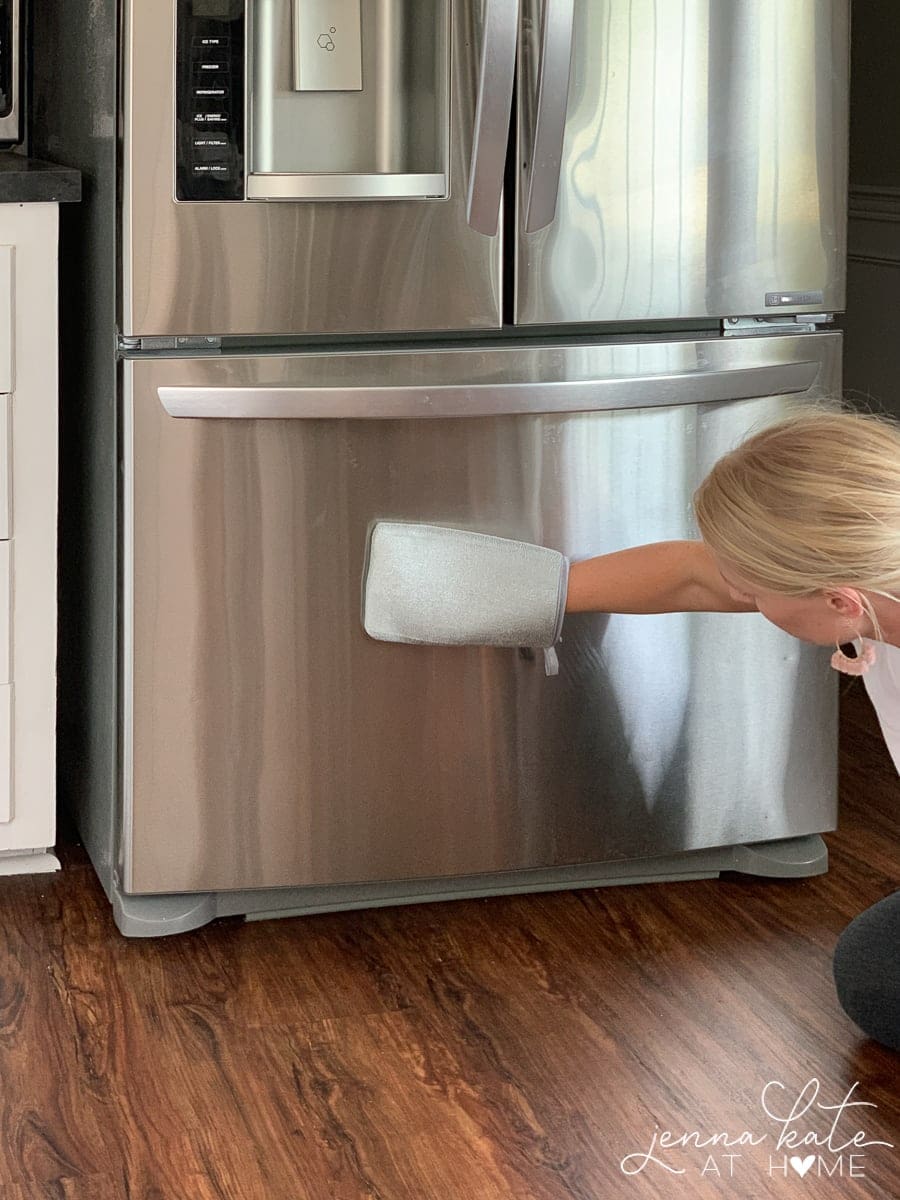 Jenna using a microfiber mitt to wipe the surface of a stainless steel fridge
