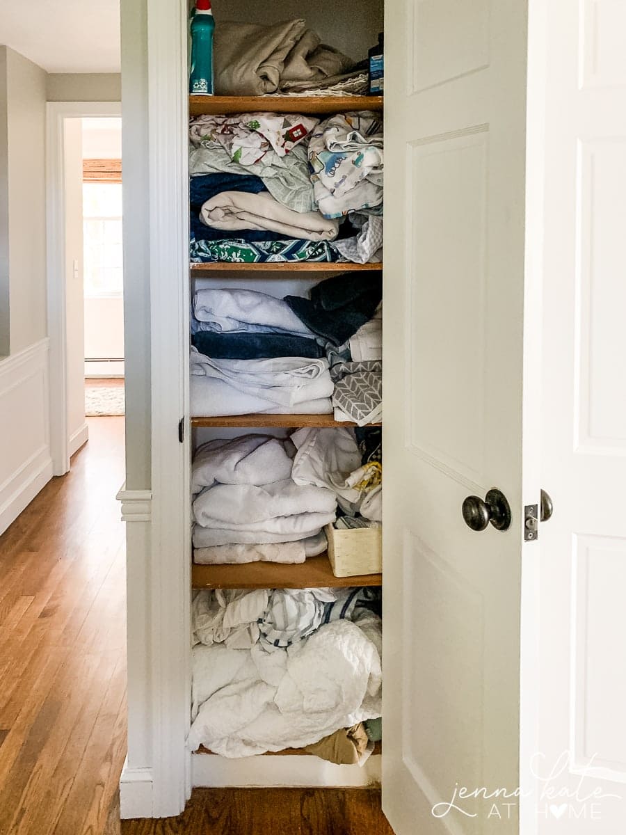 A narrow closet containing a messy assortment of towels and linen