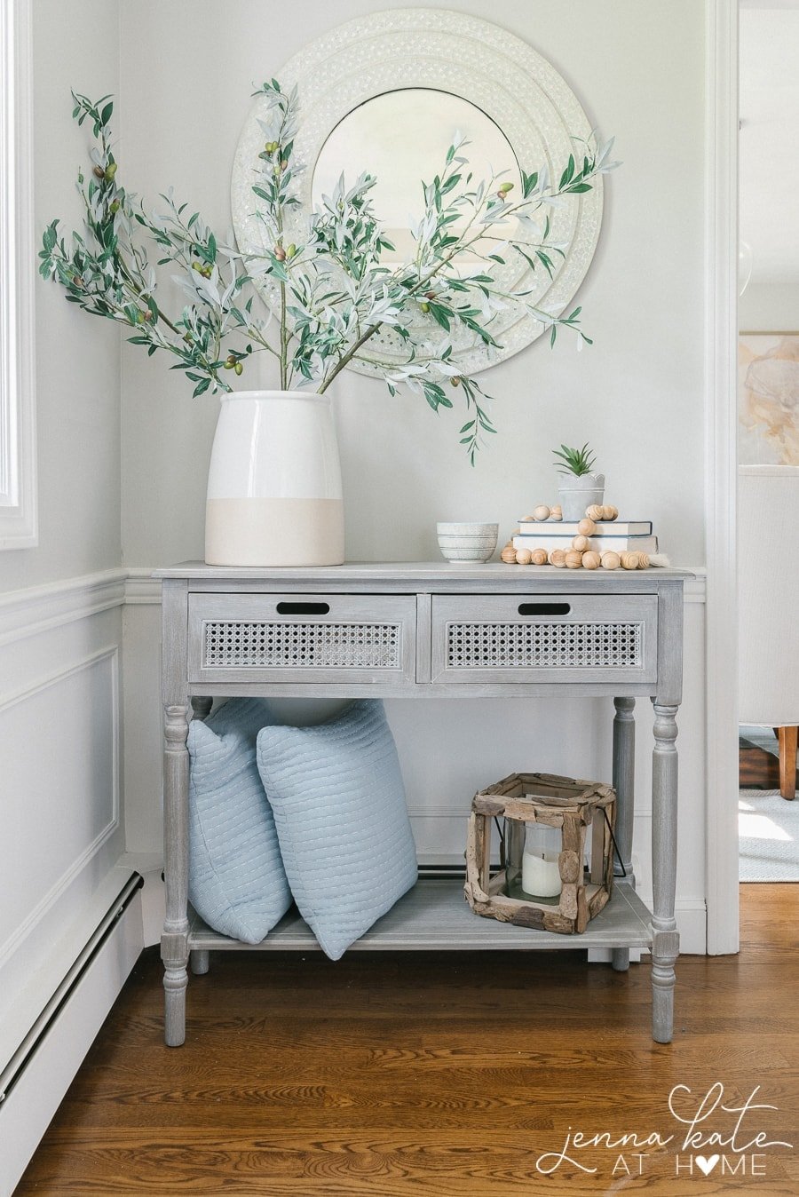 gray entryway table with large vase of stems and books stacked to the side