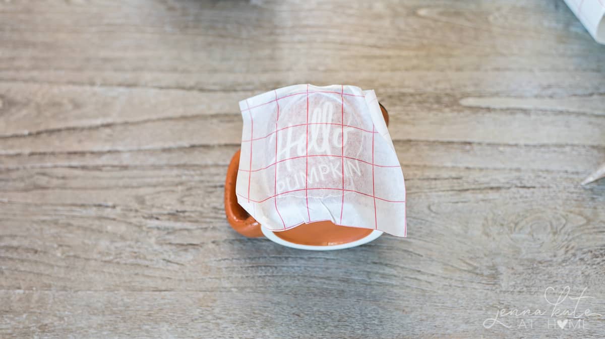 Transferring of the lettering to the mug in progress; transfer paper still attached to mug with lettering showing beneath.