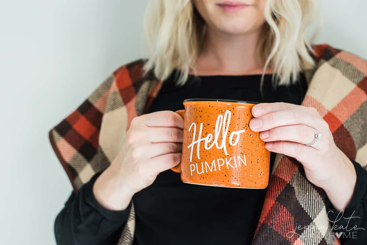 Author, wearing seasonal fall wrap, holding finished DIY mug with vinyl lettering "Hello Pumpkin"