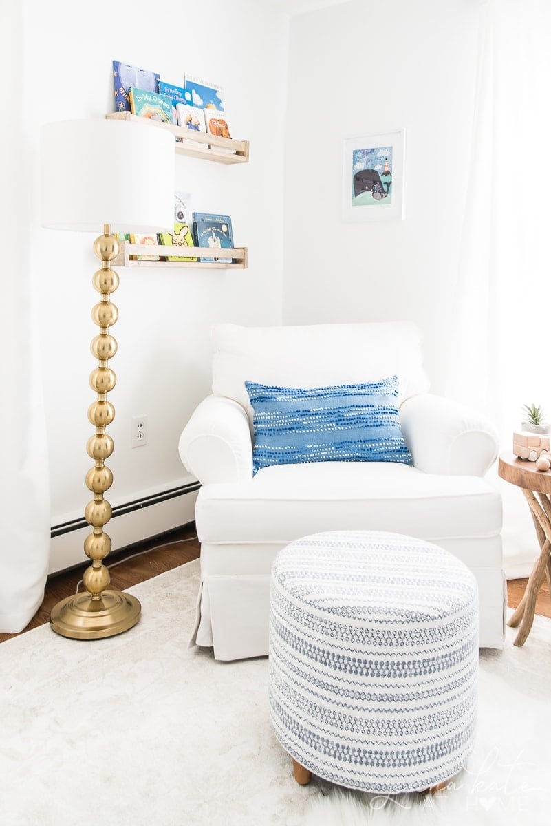 White nursery rocking chair with gold lamp and blue pillow and foot stool