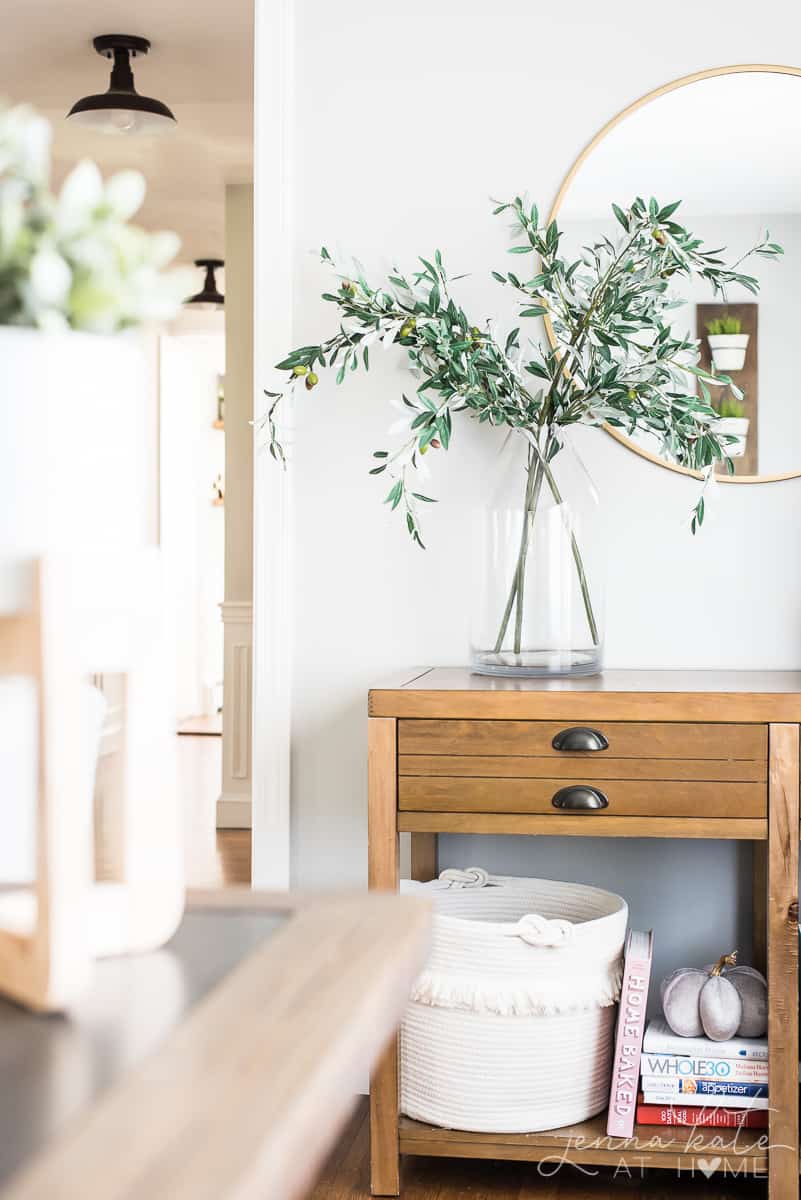 A living room with a console table and large vase filled with olive branches