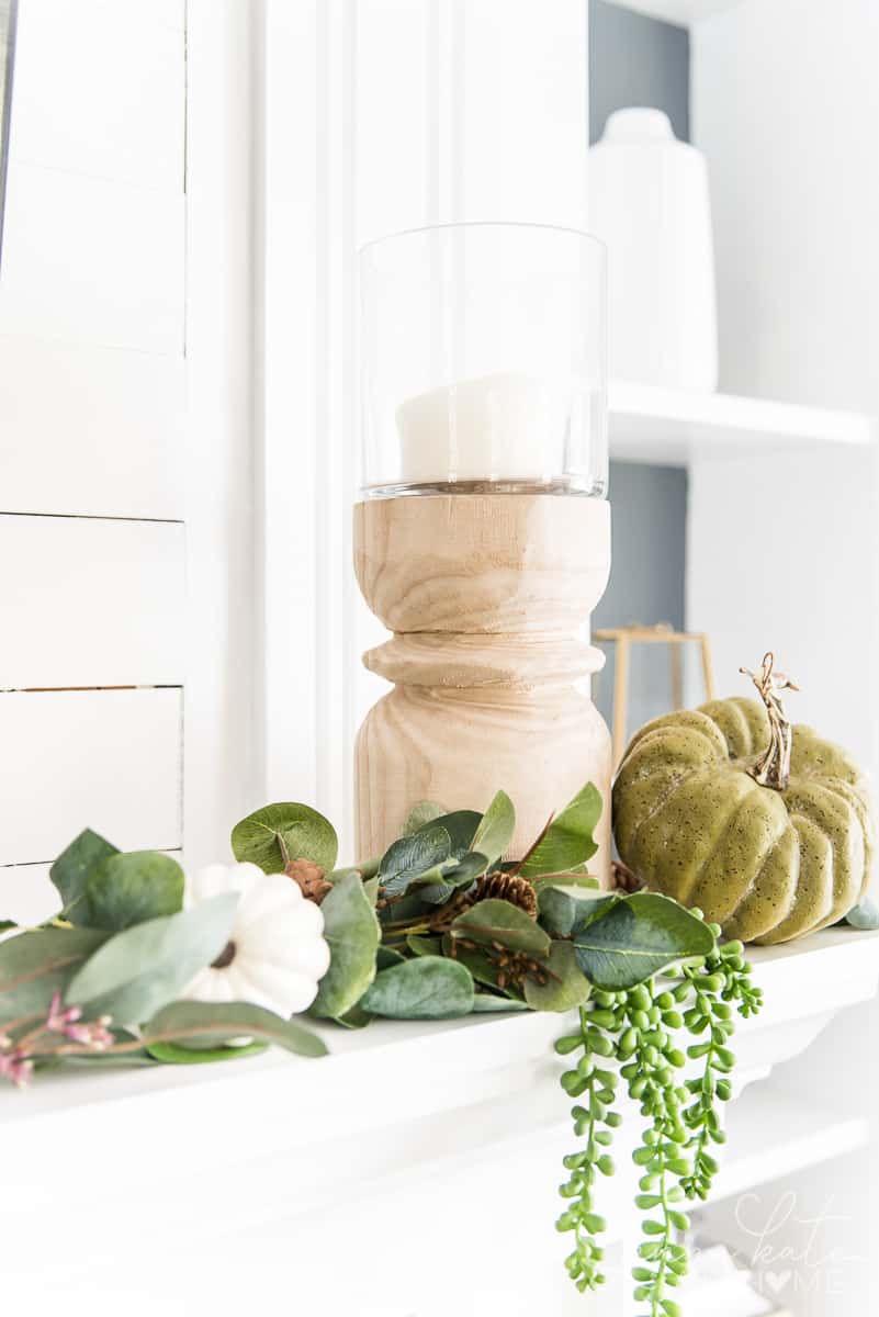 Wooden hurricane candle holder with faux greenery and pumpkins on a mantel