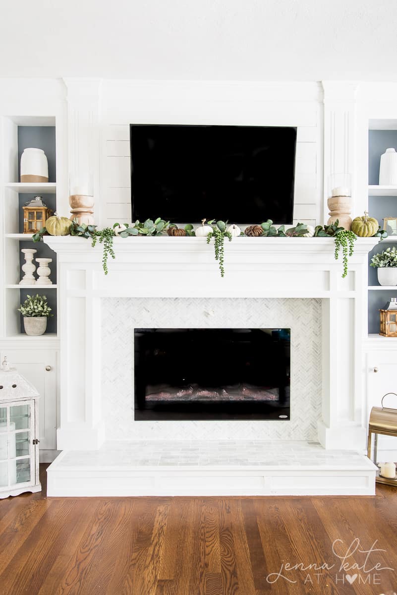 Mantel decorated for fall with draping greenery, green pumpkins and touches of natural wood