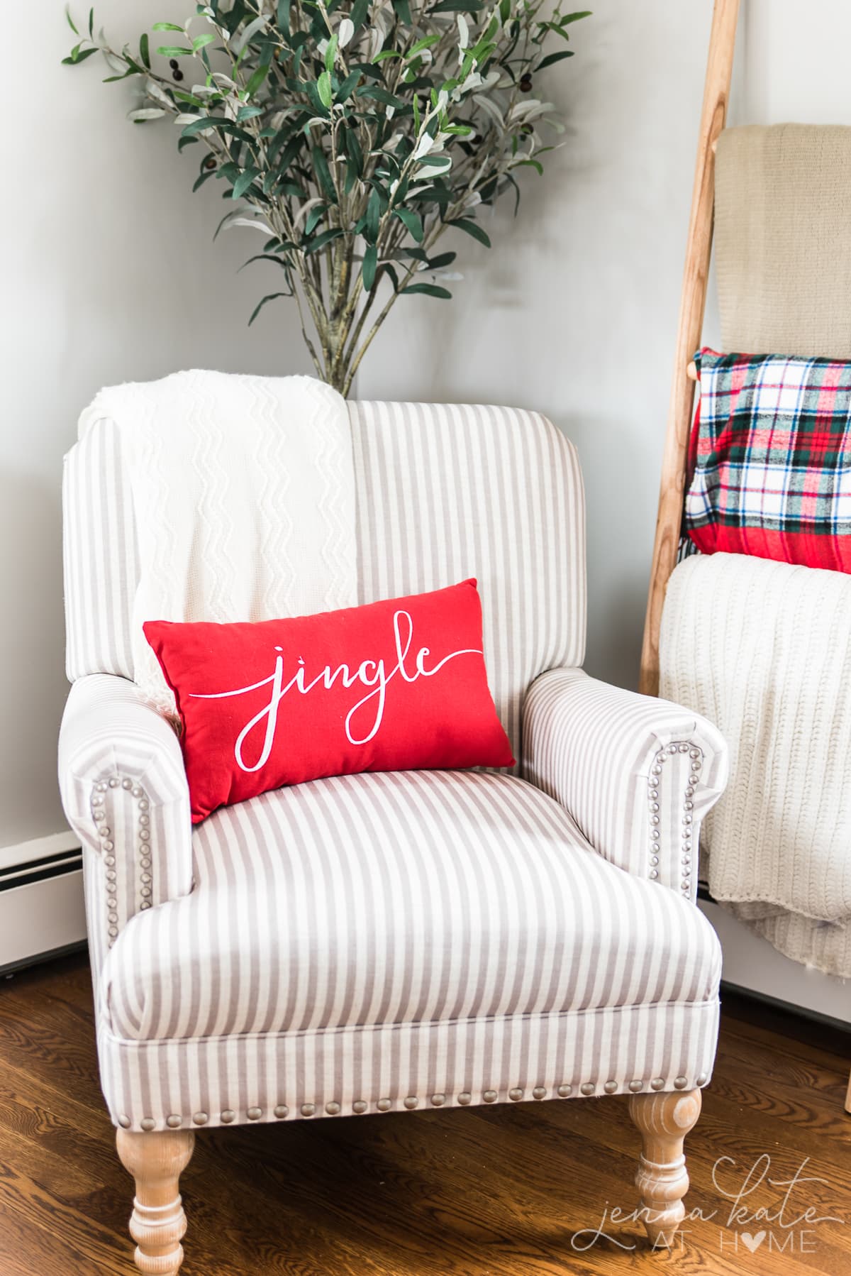 Arm chair in the corner of a room with a red pillow that reads \"jingle\"