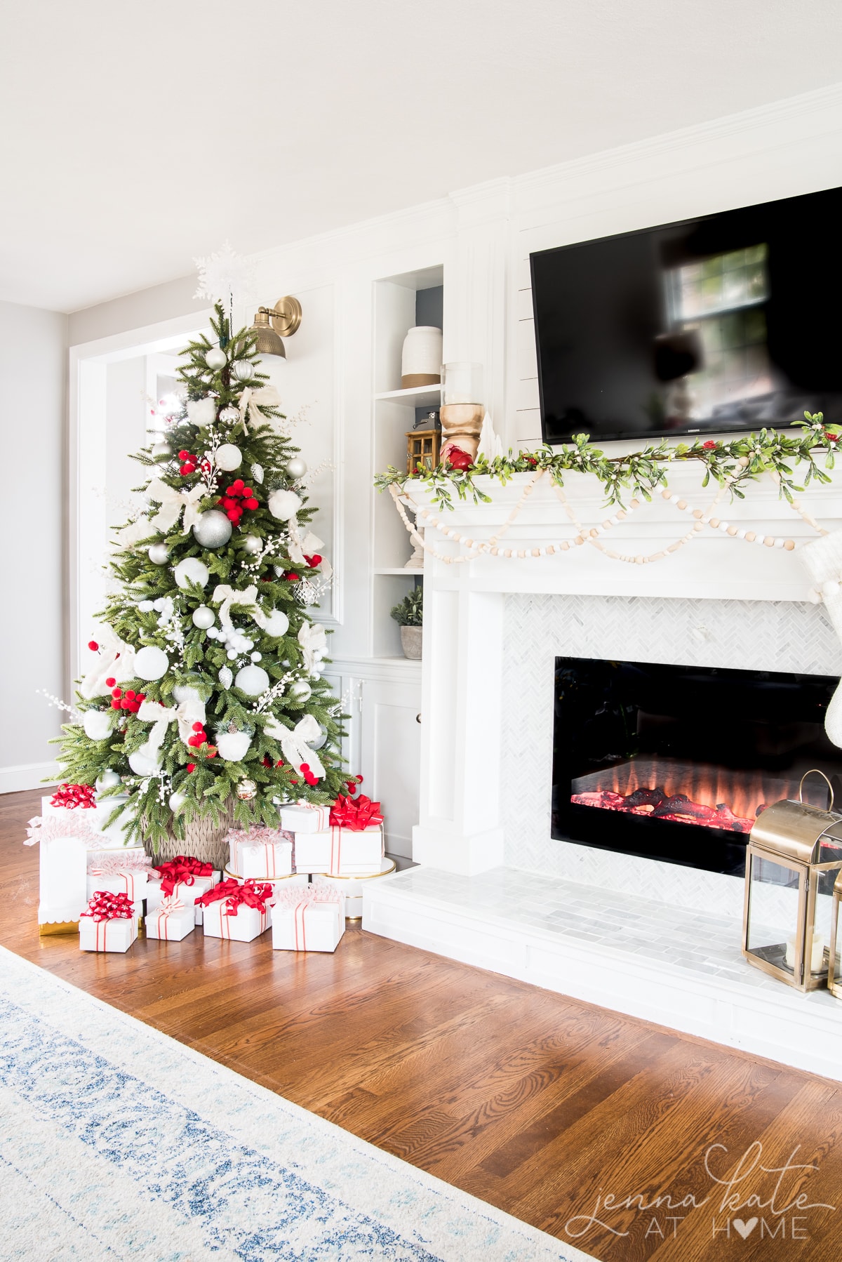 Living room fireplace mantel and Christmas tree decorated in shades of white and red