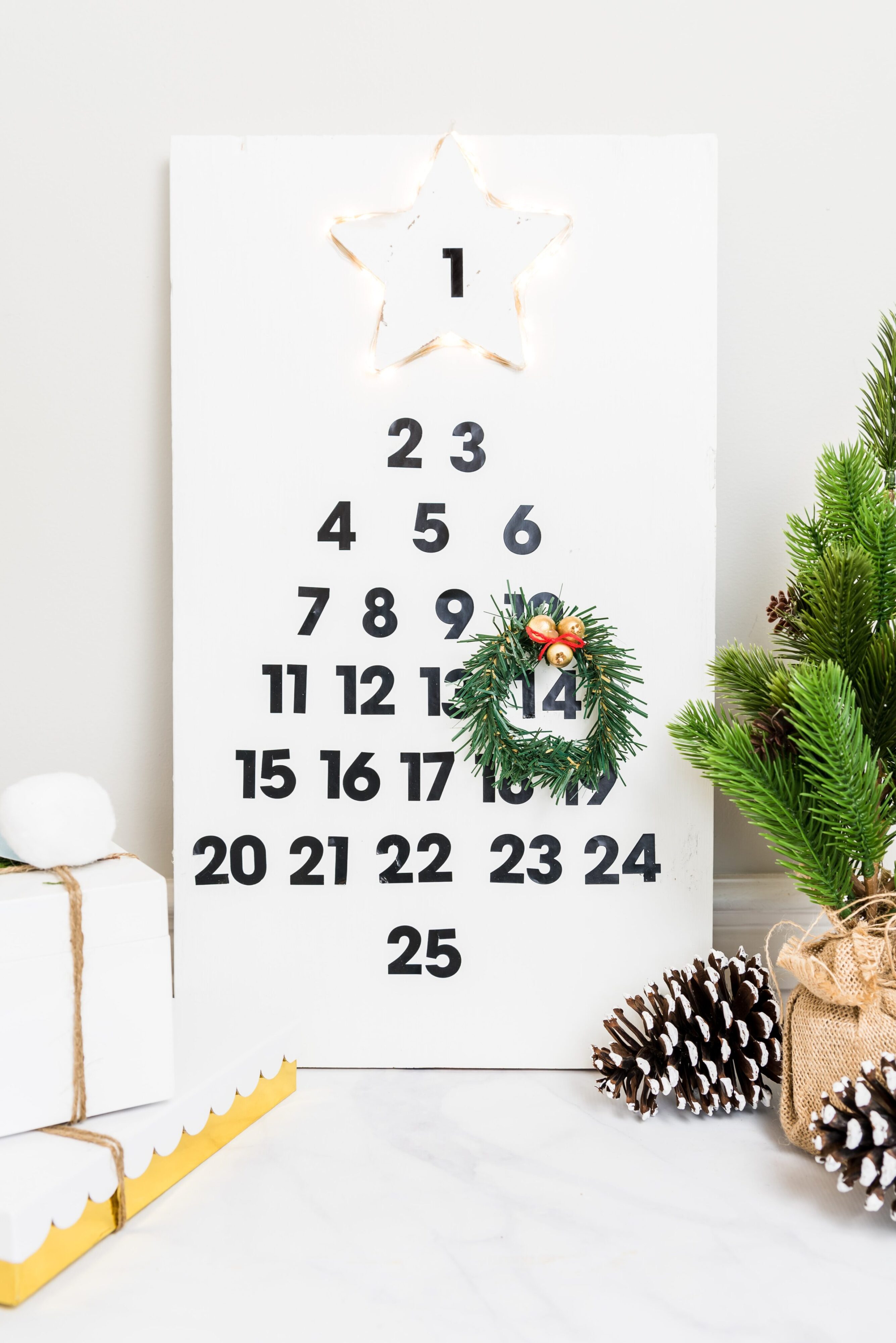 DIY wooden advent calendar featuring sticker black numbers, a homemade garland wreath, and a lit up star.