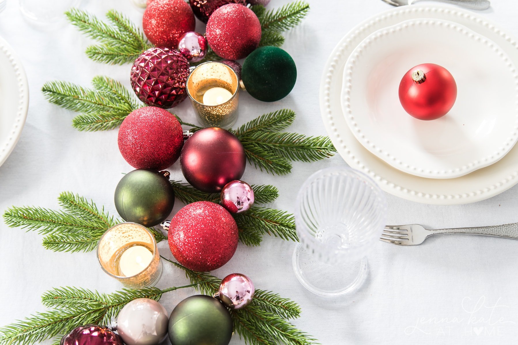 Festive Christmas table centerpiece using tree ornaments, votives and greenery