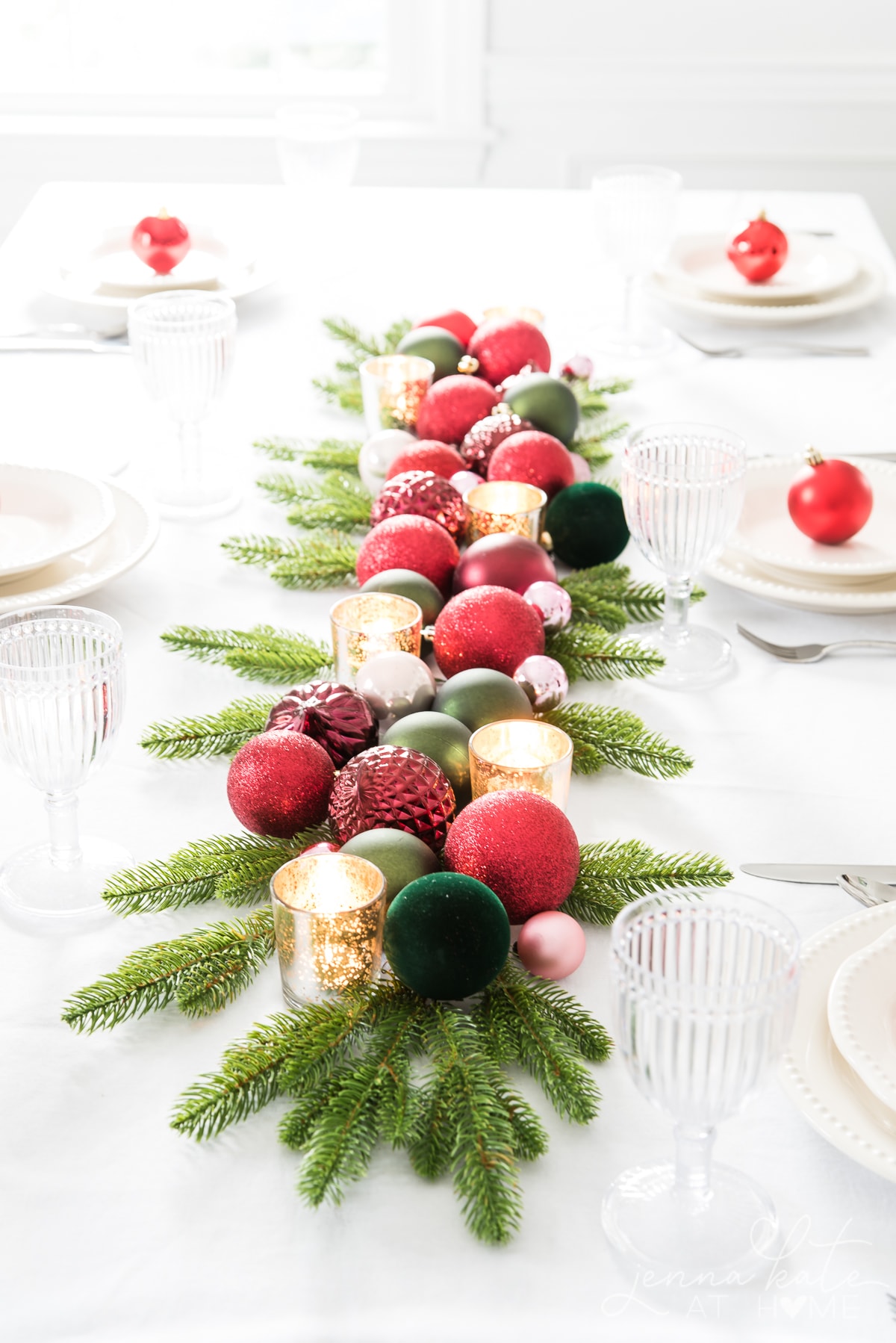 red and green Christmas ball ornaments on a table with gold votive candle holders and artificial greenery