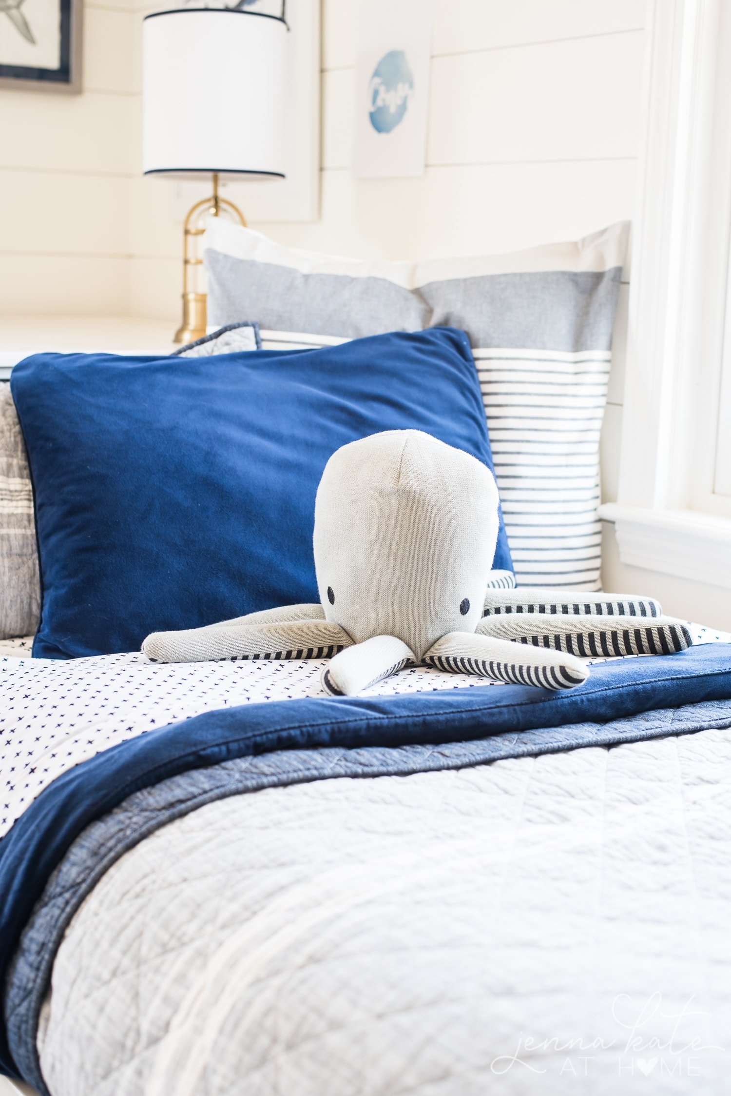 A bed with blue and white bedding, near a window, with a large plush octopus on top