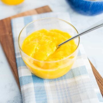 A bowl of lemon curd sitting on a table with a spoon in it