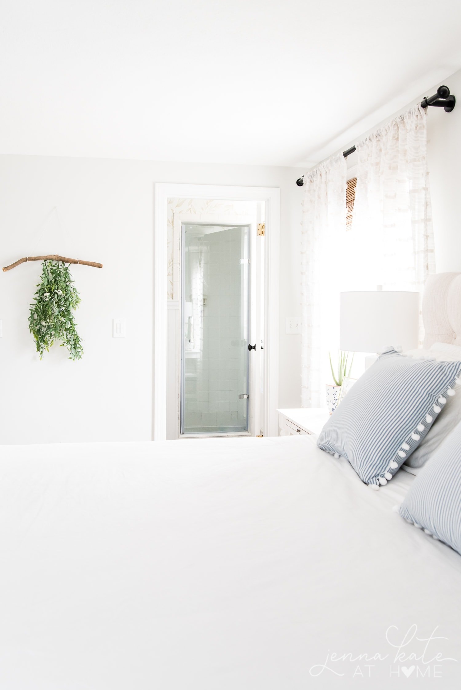 a. bright bedroom with a white comforter, blue striped pillows, and light decor on the walls.