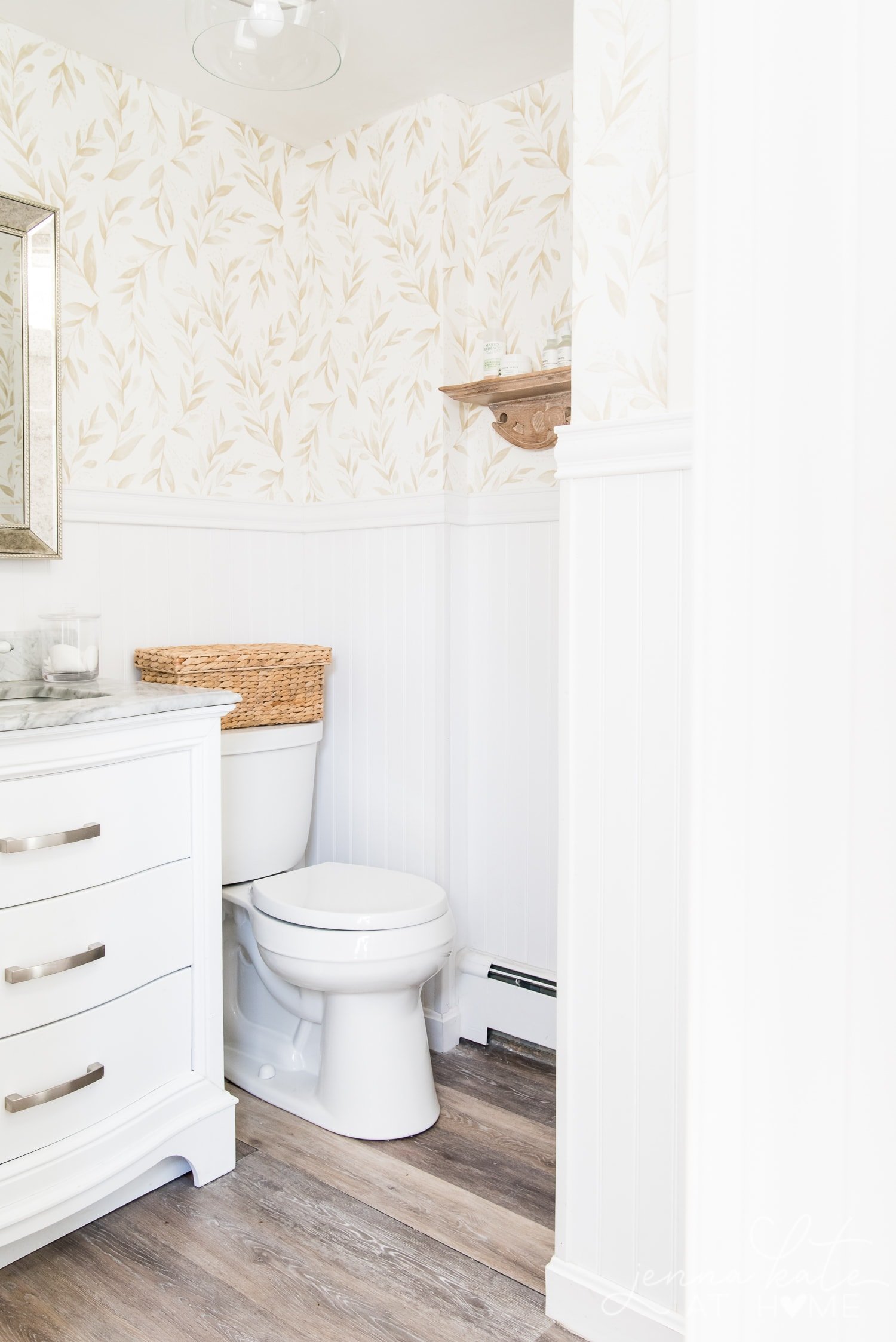 View of bathroom from another angle. Here you can see the toilet with wicker basket on top as well as the beadboard and wallpaper on the walls.