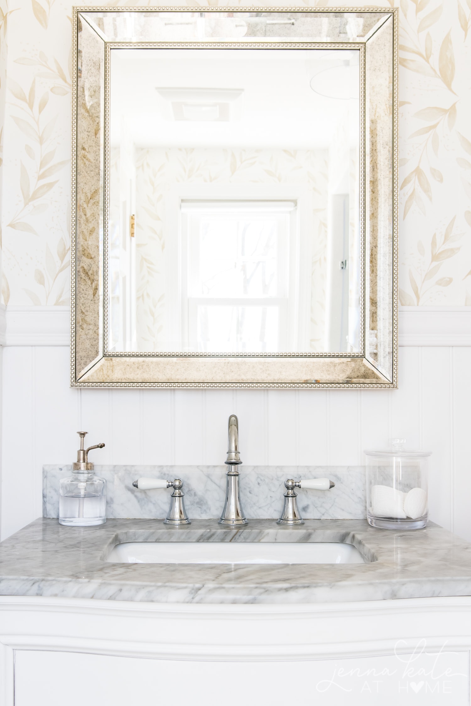 Reflection of bathroom in the mirror over the marble topped vanity with chrome faucets.