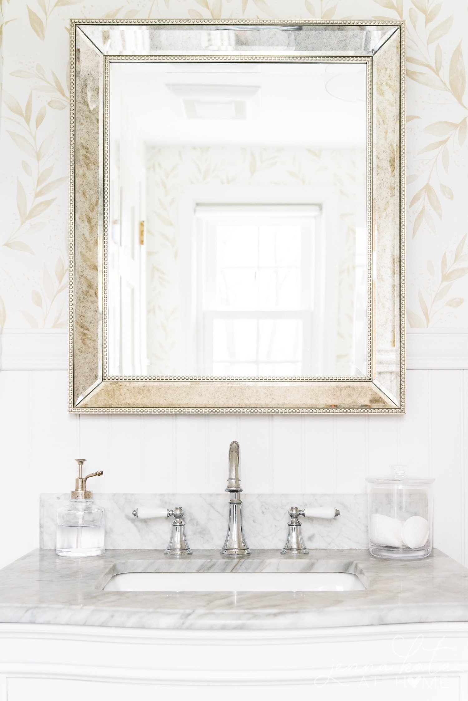 Mercury glass mirror reflecting beautiful floral wallpaper in bathroom