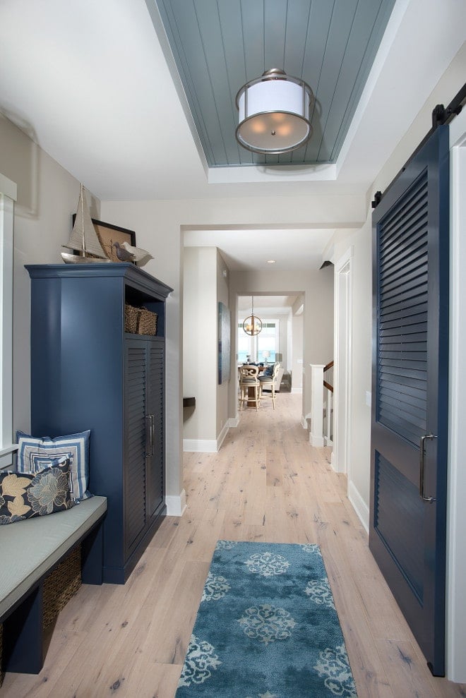 A hallway of a coastal beach home featuring Benjamin Moore\'s Revere Pewter on the walls, contrasting with the deep blue of a large cabinet and doors