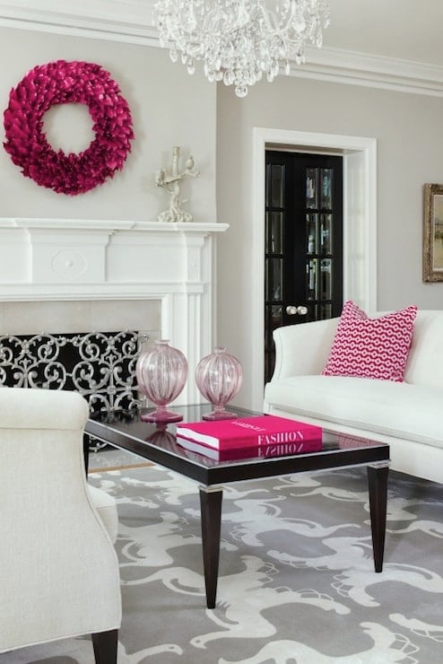 White sofa and chair with a shiny black coffee table in front of a fireplace; accentuated with pink accessories.