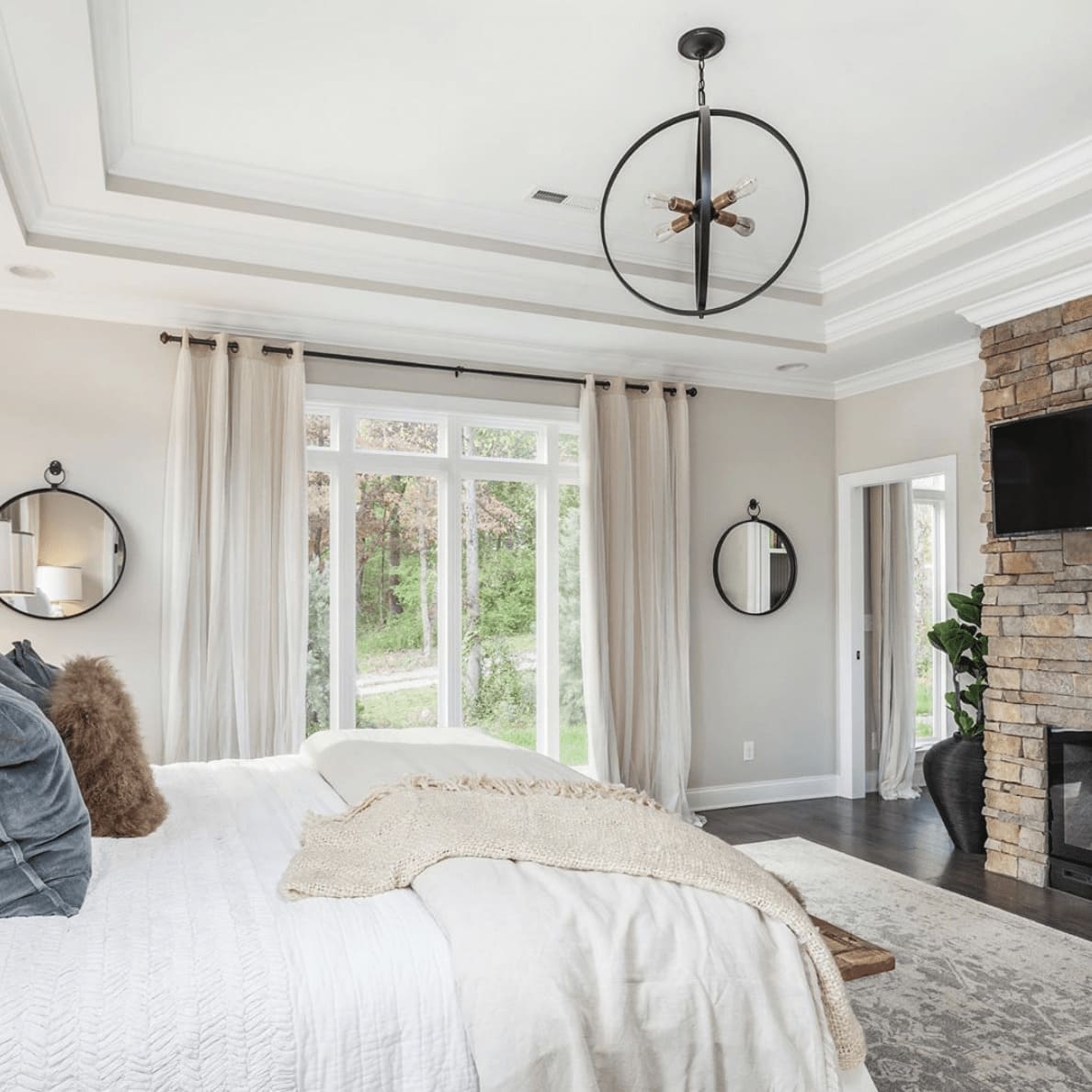 A bedroom with a brick fireplace, a large window, and a bed with decorative pillows and blankets on top