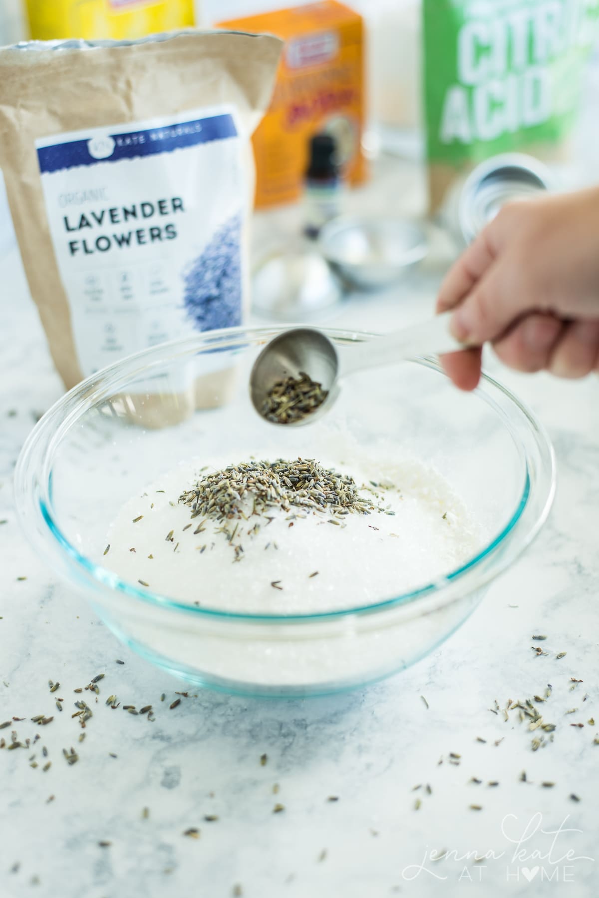 Adding a tablespoon of lavender flowers to a glass bowl  containing baking soda and other dry ingredients