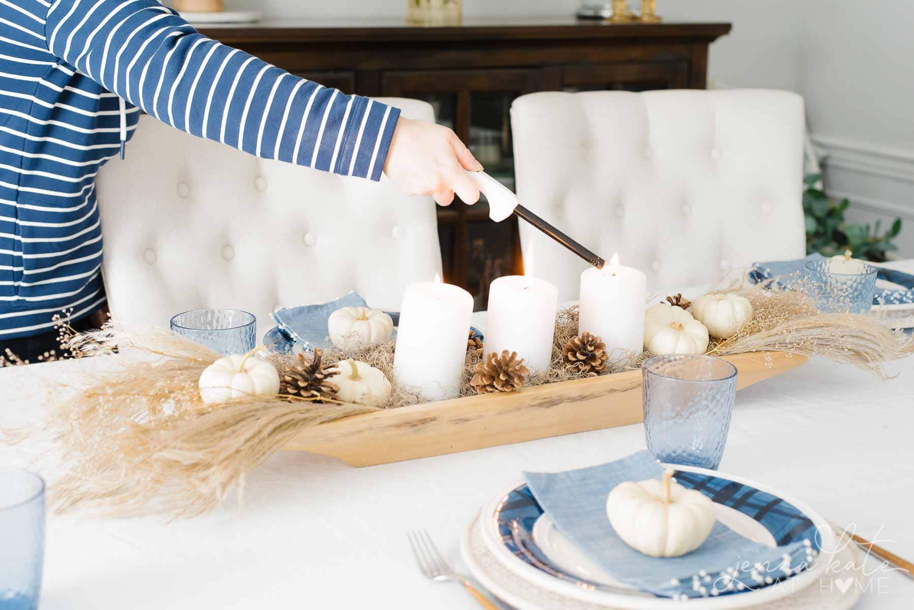 A person lighting candles on a fall centerpiece