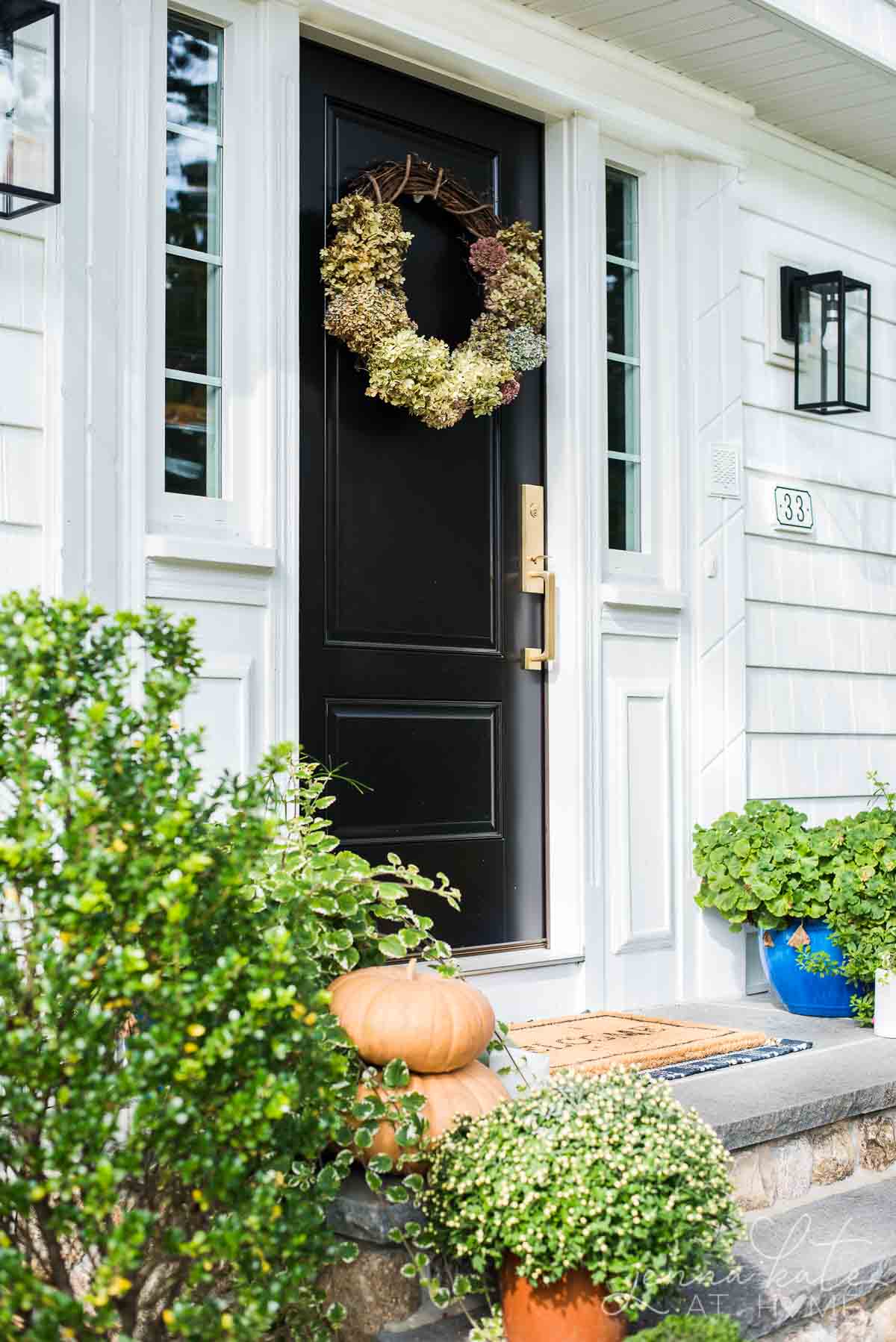 minimalistic fall front porch with pumpkins, fall wreath, and welcome mat.